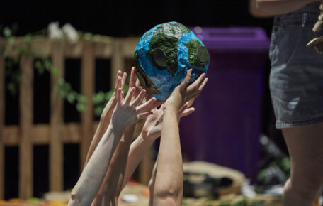 A papermache earth being held up by several pairs of hands.