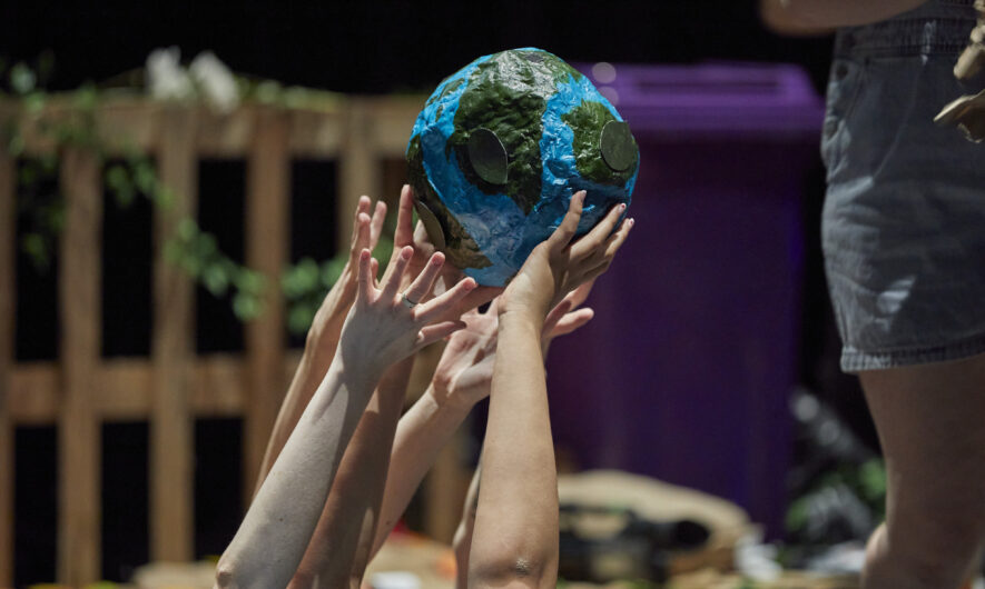 A papermache earth being held up by several pairs of hands.