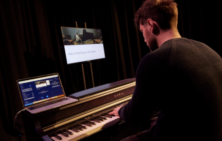 A performer at a piano with a laptop and a screen next to them,