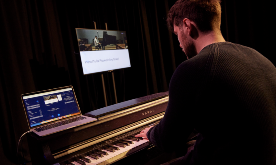 A performer at a piano with a laptop and a screen next to them,