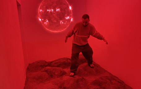 A person standing in a red small room with an uneven floor and a light globe sphere next to them.