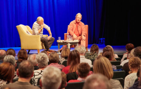 Michael Morpurgo on a stage in from of an audience seated alongside a facilitator.