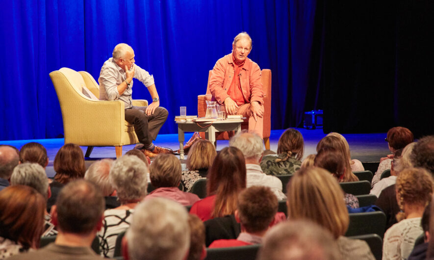 Michael Morpurgo on a stage in from of an audience seated alongside a facilitator.