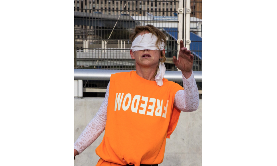 A person in an orange bib, wearing a blindfold.