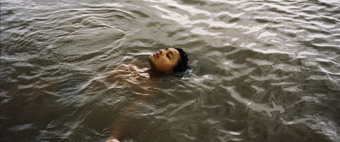Young person floats in dark water with their face out of the water and eyes closed.