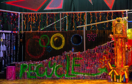 photograph of The Spongebob Musical set. A wall built out of recycled cans is spray-painted in vibrant colours and has 'Recycle' written across it.