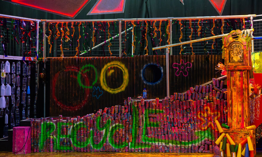 photograph of The Spongebob Musical set. A wall built out of recycled cans is spray-painted in vibrant colours and has 'Recycle' written across it.