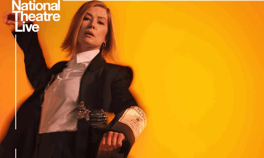 Rosamund Pike poses against a orange background with her right arm stretched up into the air. She wears a black suit with a white shirt and has a blond bob hair style. Inter Alia is written in capitol letters on the background.