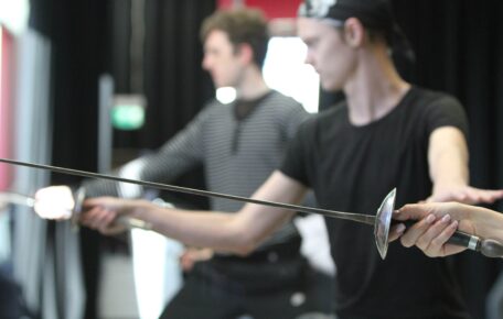 two young men hold a fencing sword in front of themselves and hold combat pose.