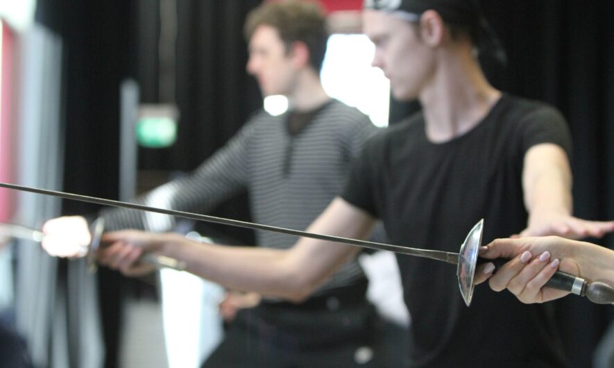 two young men hold a fencing sword in front of themselves and hold combat pose.