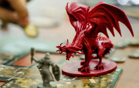 Image depicts a table set up for playing a game of D+D with dice, counters and a dragon figure in the centre.
