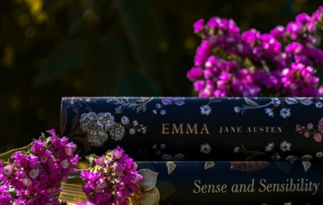 A series of Austen novels stacked ontop of each other with purple flowers surrounding the books.