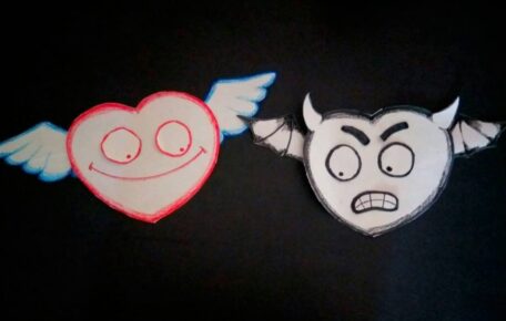 Two paper cut out hearts with wings, one with a happy face and the other with a frowny face.